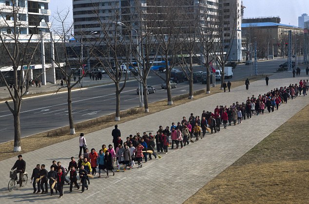 North Korean children carrying brooms help tidy up the area around bronze statues of the late leaders